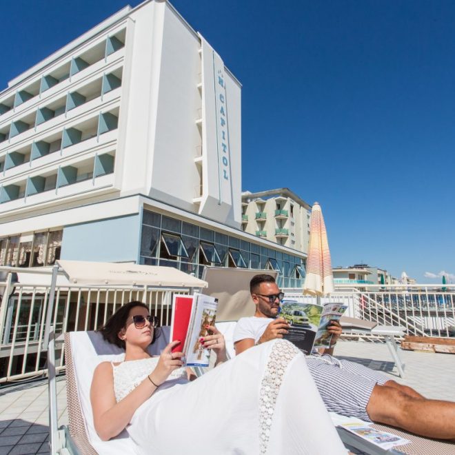 Coppia sulla terrazza, legge riviste sdraiata su comodi lettini