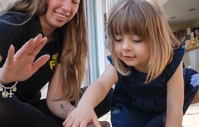 Bimba gioca con sabbia e secchiello insieme a una ragazza dell’animazione