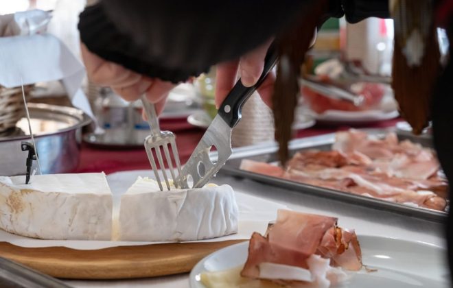 Una cliente con coltello e forchetta taglia una fetta di brie dal tavolo del buffet