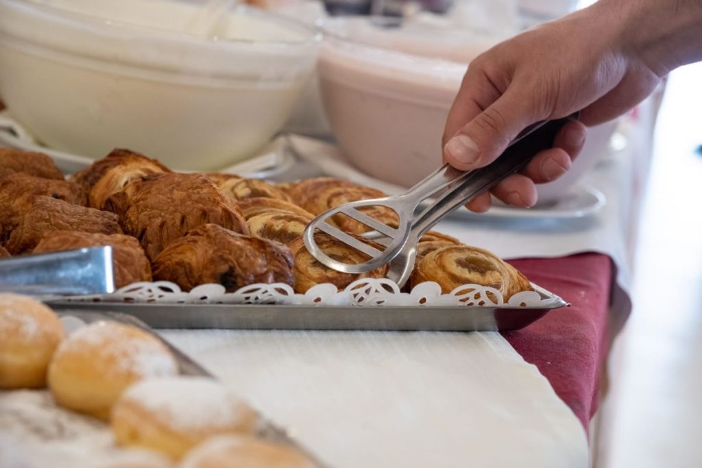 cliente raccoglie con la pinza una brioche al buffet di colazione