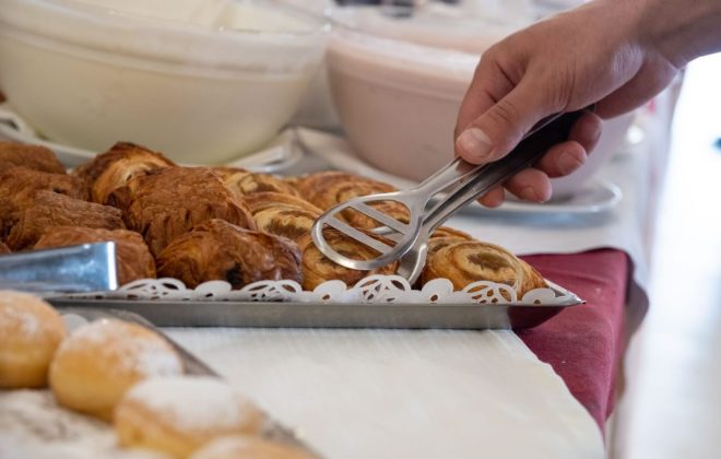 cliente raccoglie con la pinza una brioche al buffet di colazione