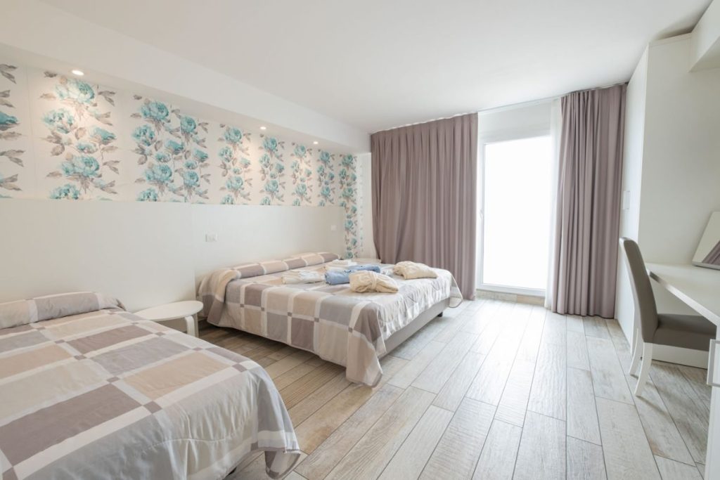 camera con letto matrimoniale e letto singolo, con carta da parati floreale, luminosa porta finestra e con accappatoio e asciugamani sui letti
