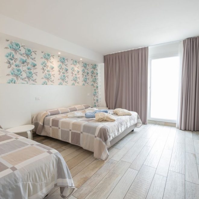 camera con letto matrimoniale e letto singolo, con carta da parati floreale, luminosa porta finestra e con accappatoio e asciugamani sui letti camera con letto matrimoniale e letto singolo, con carta da parati floreale, luminosa porta finestra e con accappatoio e asciugamani sui letti