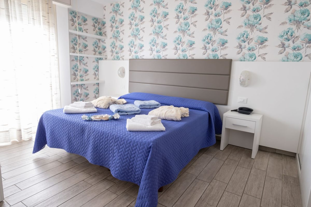 H. CAPITOL-50 camera con letto matrimoniale con carta da parati floreale, ampia porta finestra e con accappatoio e asciugamani sui letti