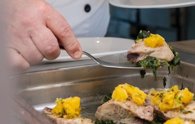 Chef raccoglie dalla teglia un cucchiaio di pesce al forno con patate e bieta saltata