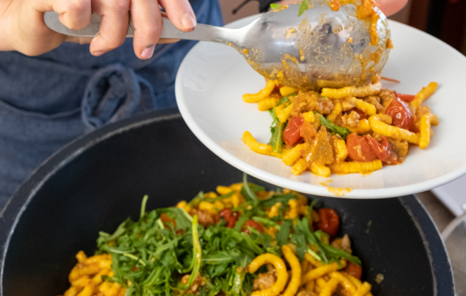addetto al buffet riempie piatto di passatelli asciutti con rucola pomodoro e pesce