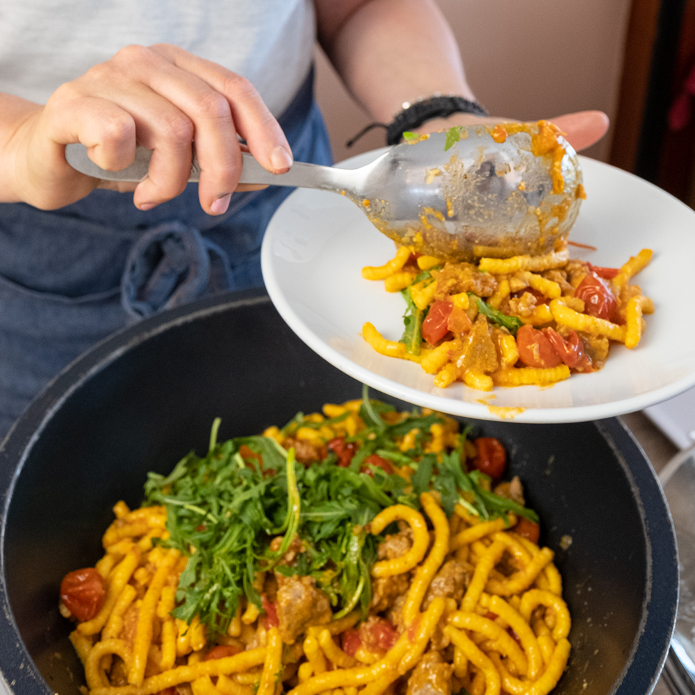 addetto al buffet riempie piatto di passatelli asciutti con rucola pomodoro e pesce
