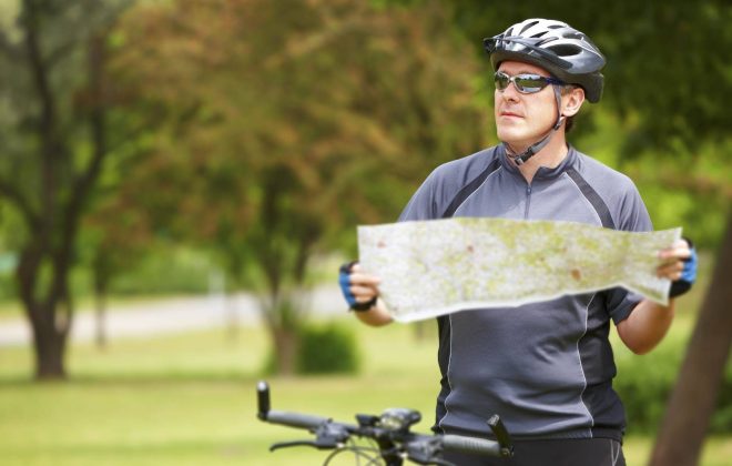 cicloamatore fermo sulla bici mentre consulta una mappa cartacea